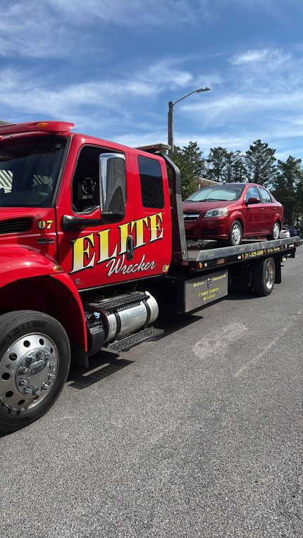 Red tow truck carrying a red pickup on a flatbed under a blue sky