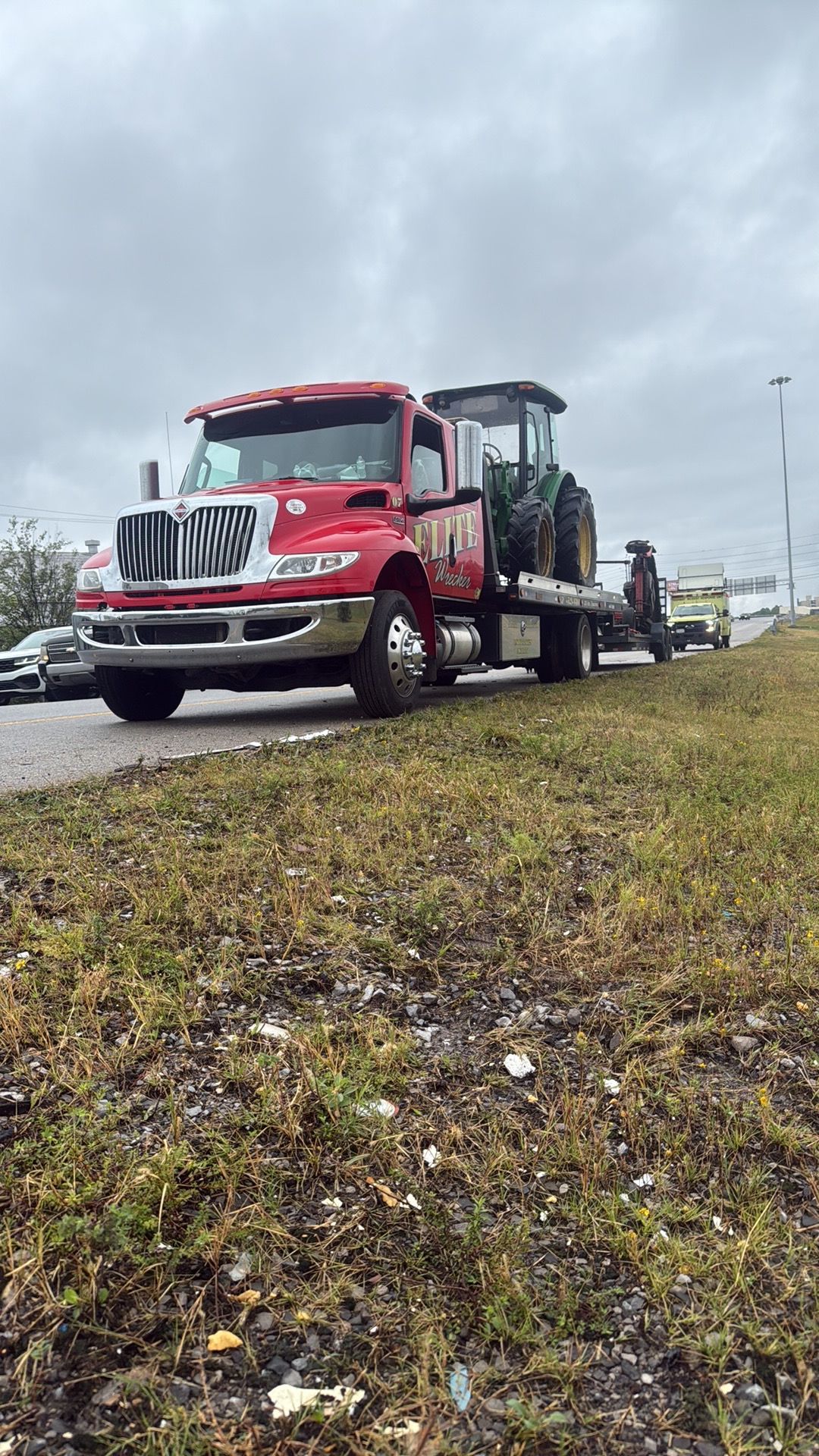 Red tow truck with a flatbed on a roadside under cloudy skies