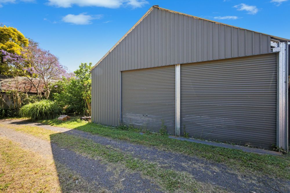 Metal shed with large roller doors beside a gravel driveway on a sunny day