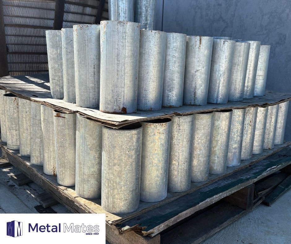 Stacked gray metal fence posts on pallets outdoors in a yard.