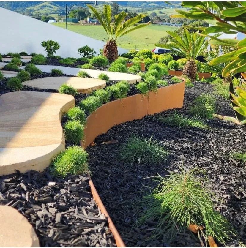 Curved stone garden path beside tropical plants and mulch, overlooking a landscaped hillside view