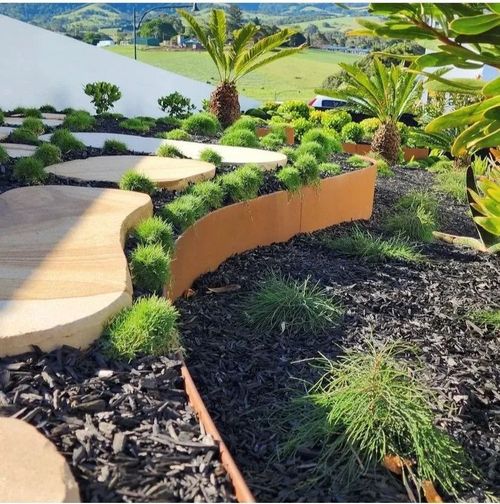 Curved stone garden path beside tropical plants and mulch, overlooking a landscaped hillside view