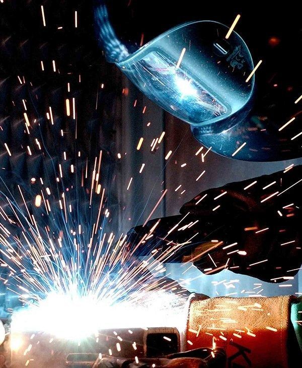 Bright welding sparks fly from a metalwork torch near a blue protective helmet.