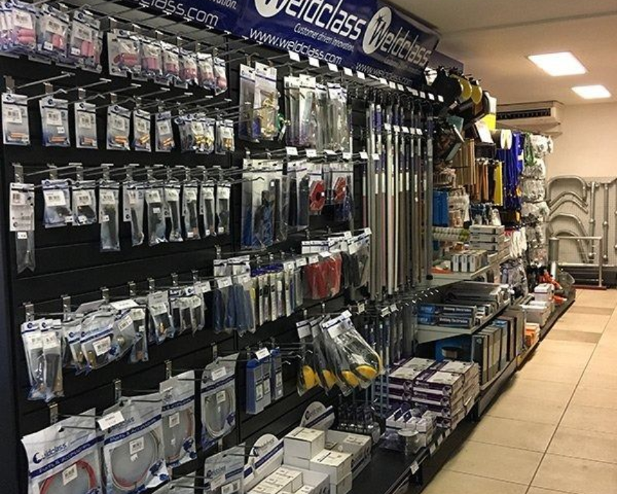 Store aisle with hanging accessories and hardware supplies on shelves, under bright indoor lighting.