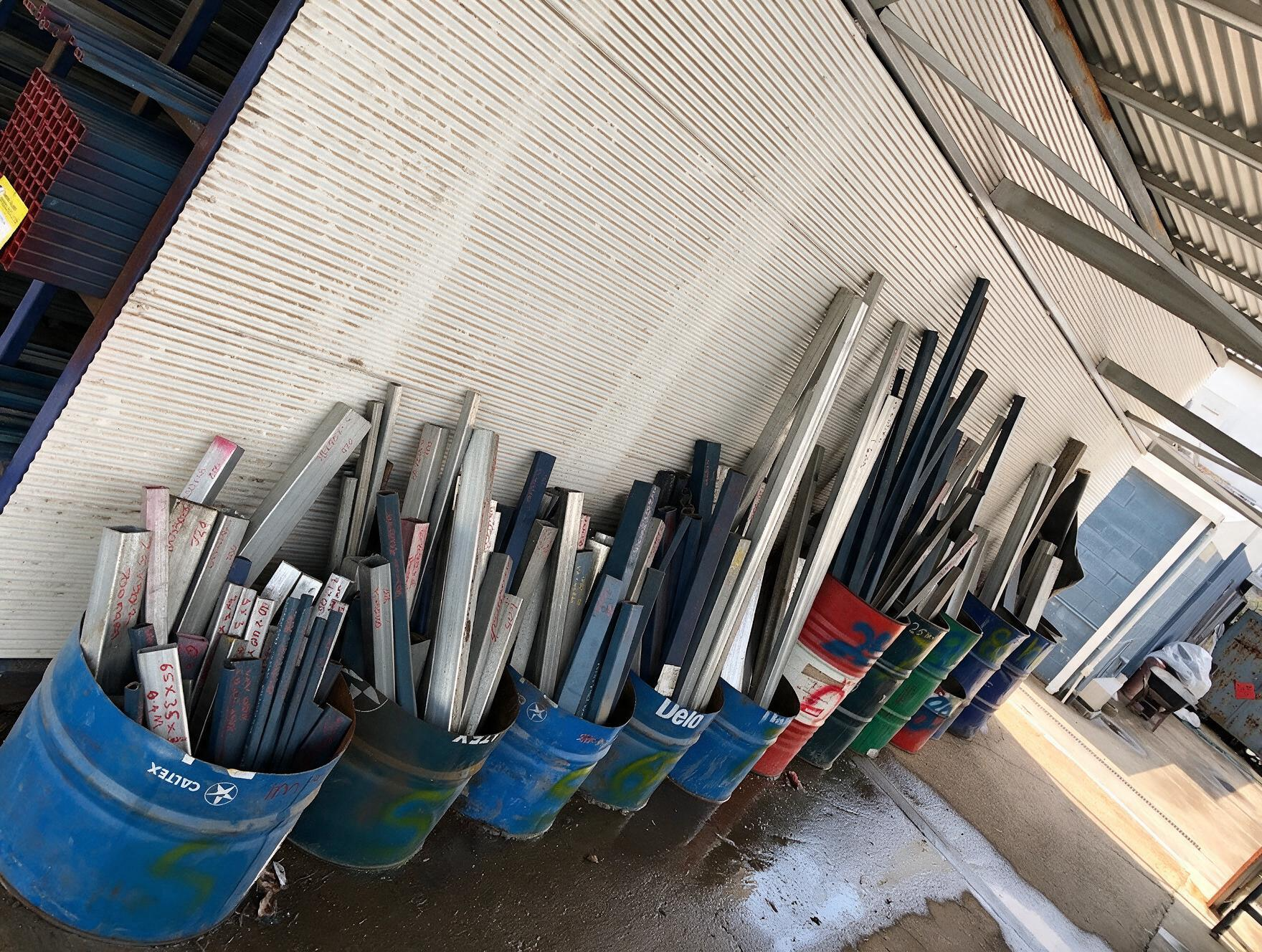 Blue buckets filled with long metal rods leaning beside a white wall outdoors