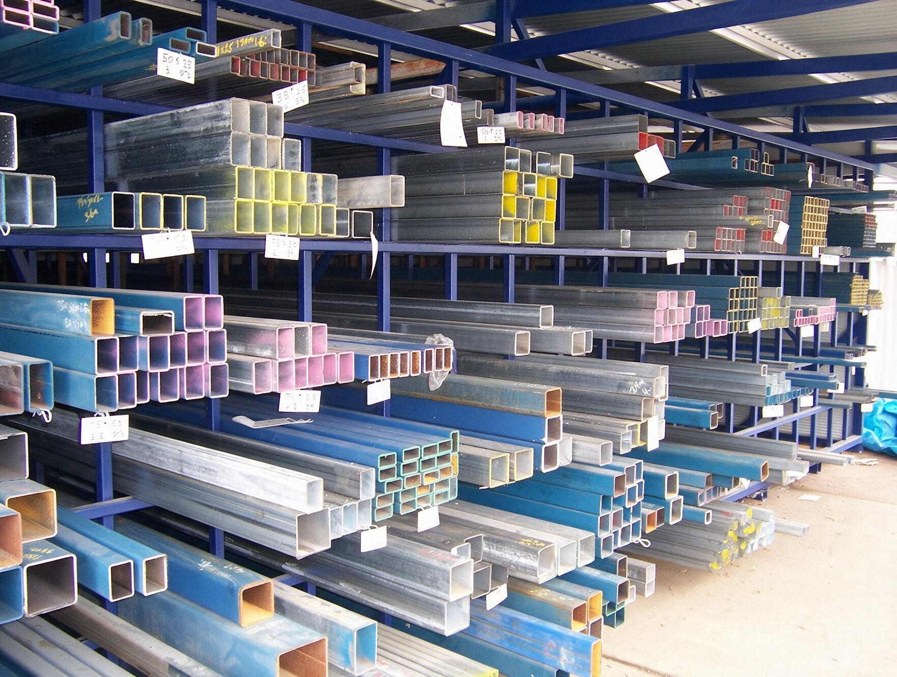 Stacks of colorful metal beams and tubing stored on warehouse racks indoors