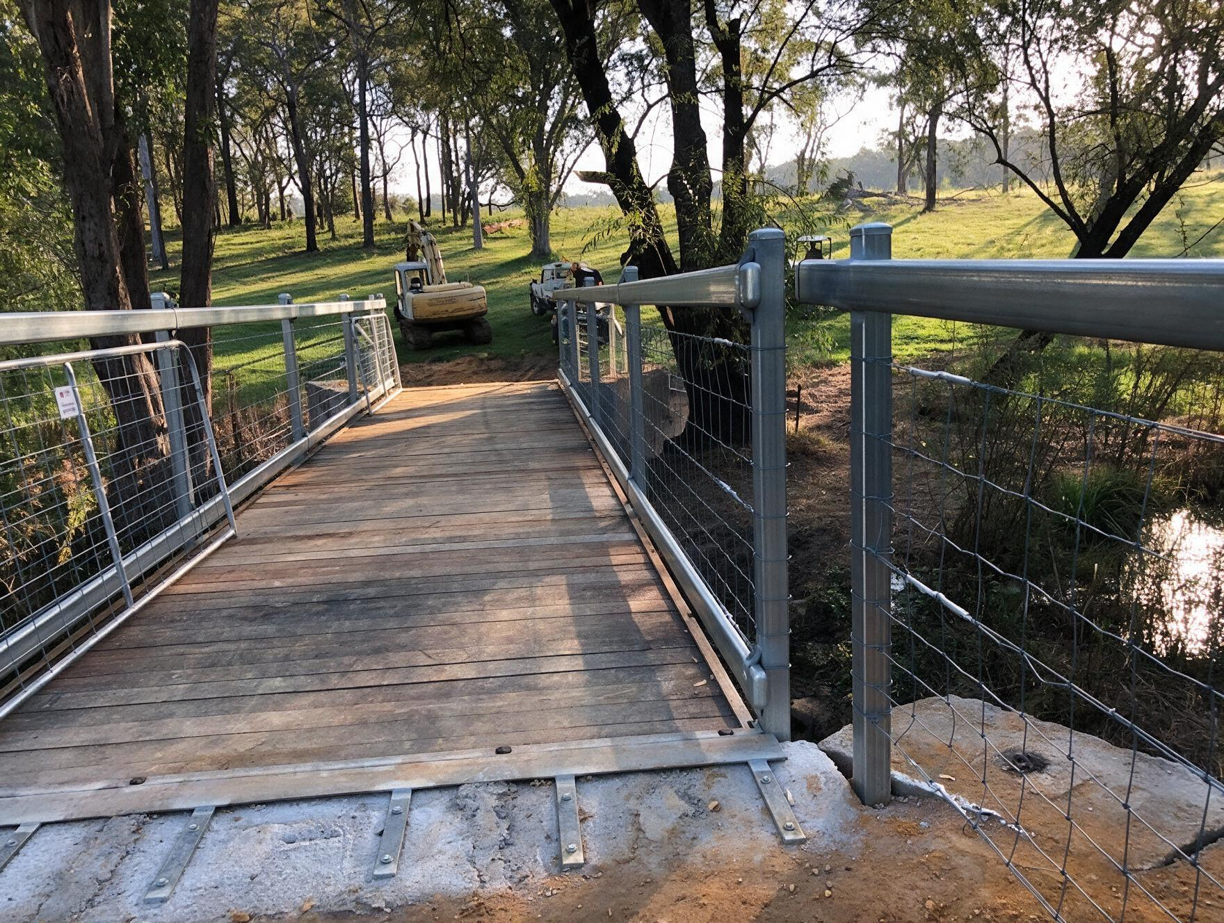 Wooden pedestrian bridge with wire railings crossing a wooded creek in a park