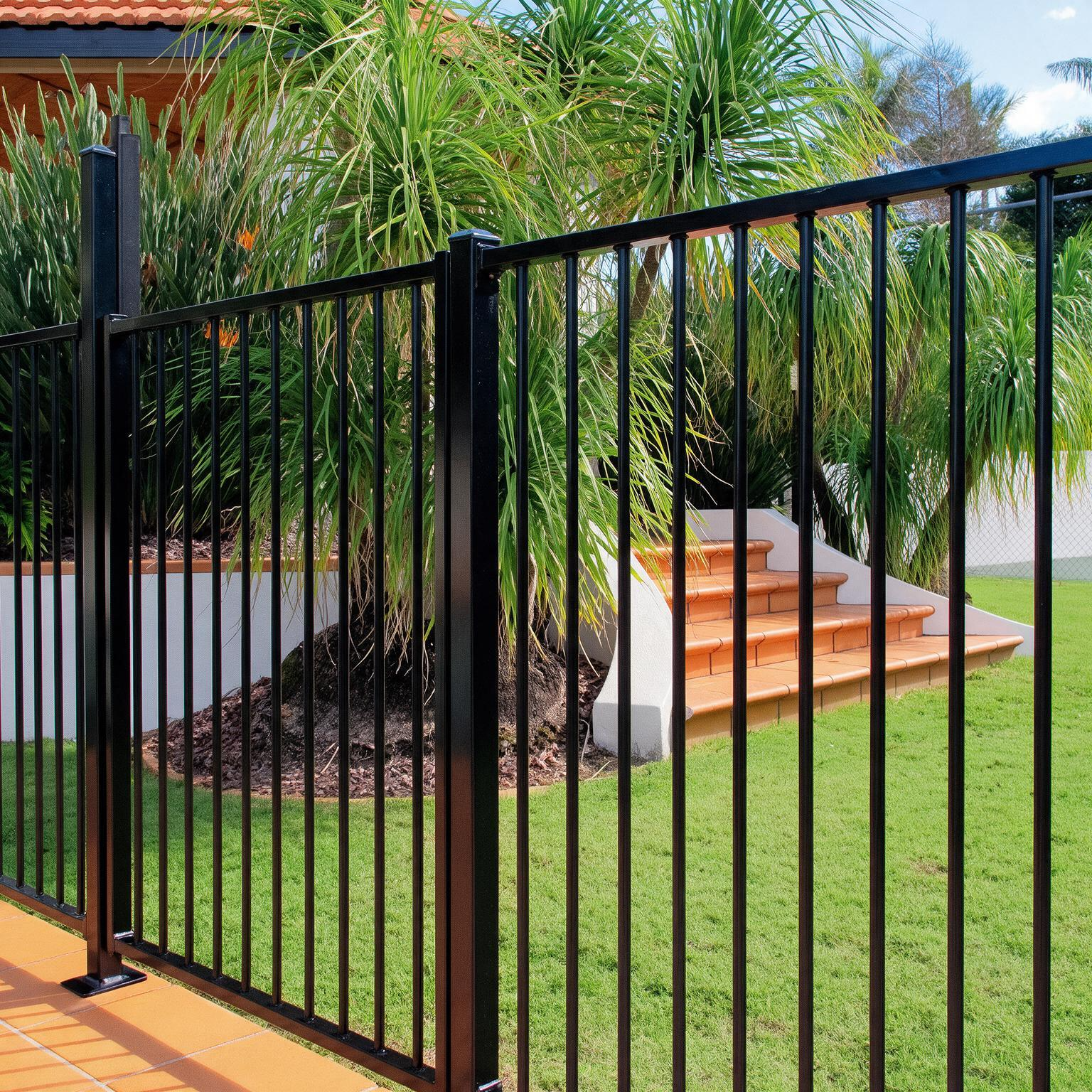 Green metal fence along a grassy path in a sunny outdoor area