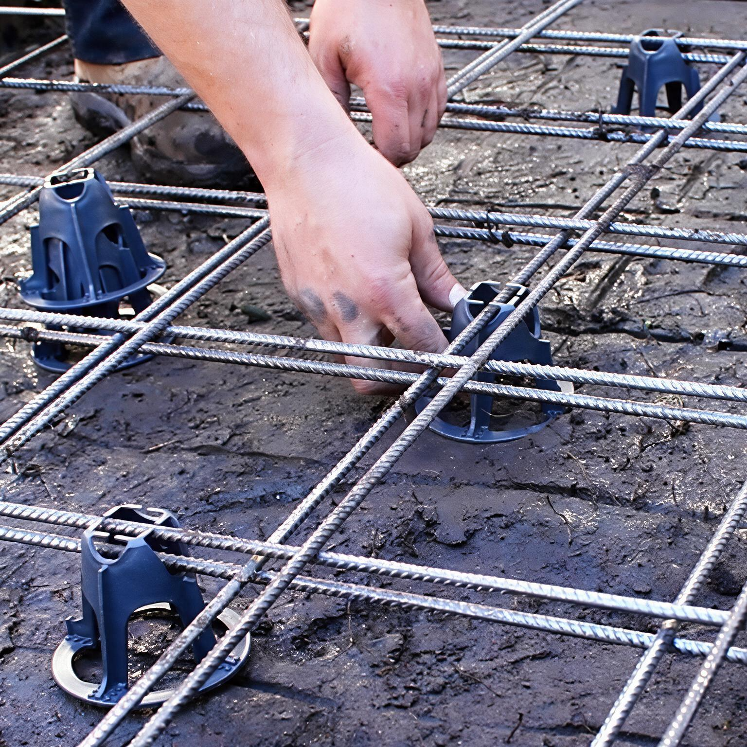 Hands placing plastic spacers in a rebar grid over wet concrete.