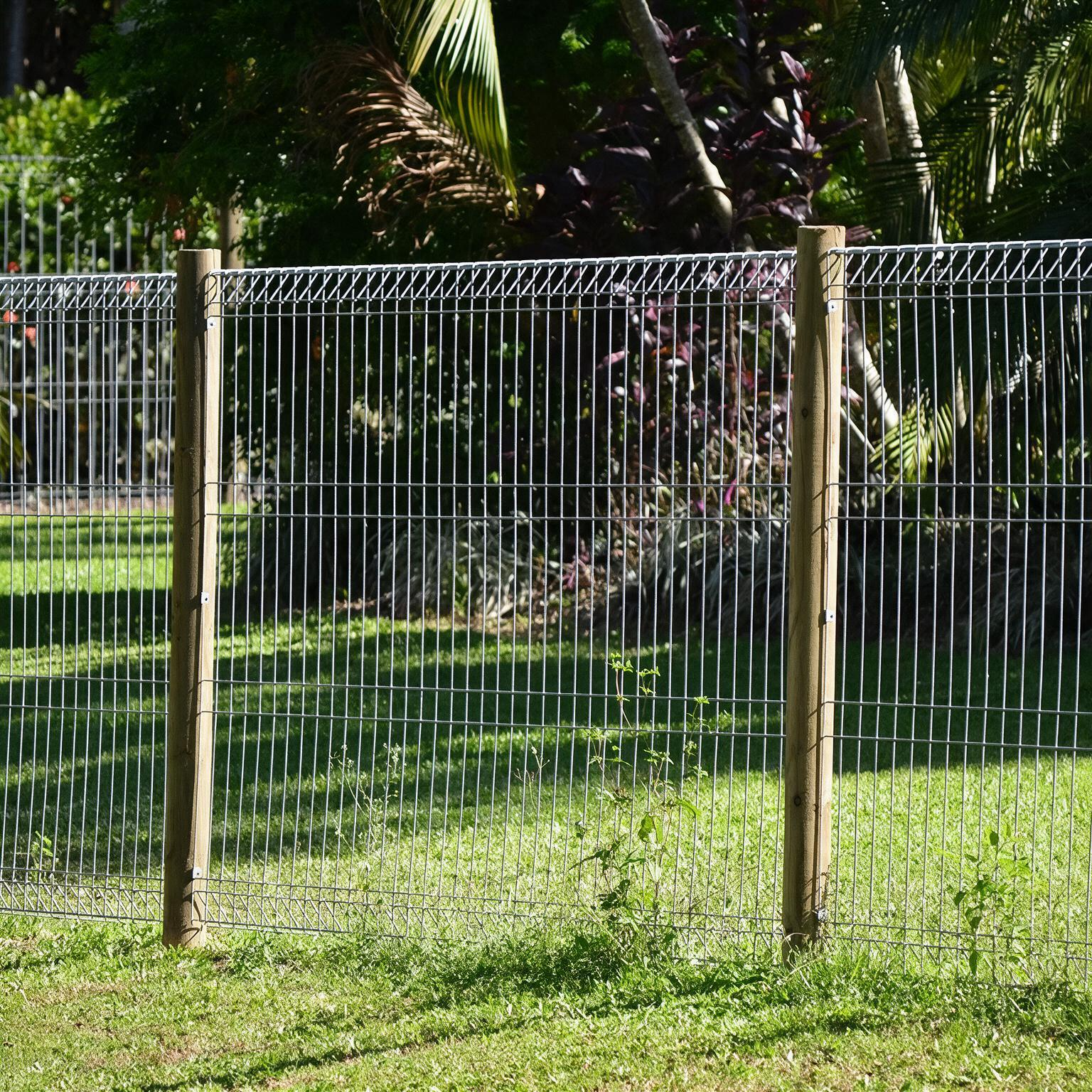 Silver metal fence gate beside a white building and grassy yard under a blue sky