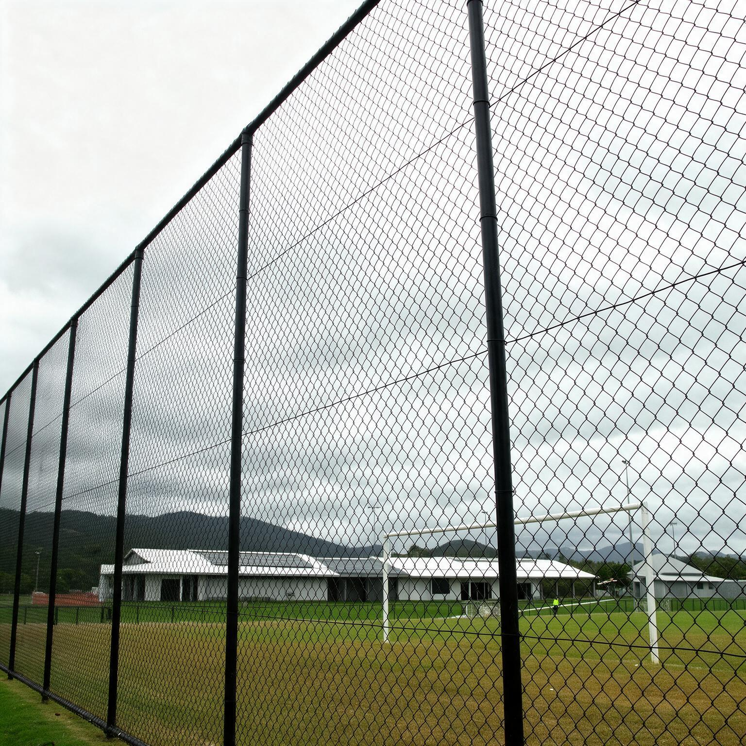 Two uniformed workers standing by a chain-link fence near a truck in a grassy field.