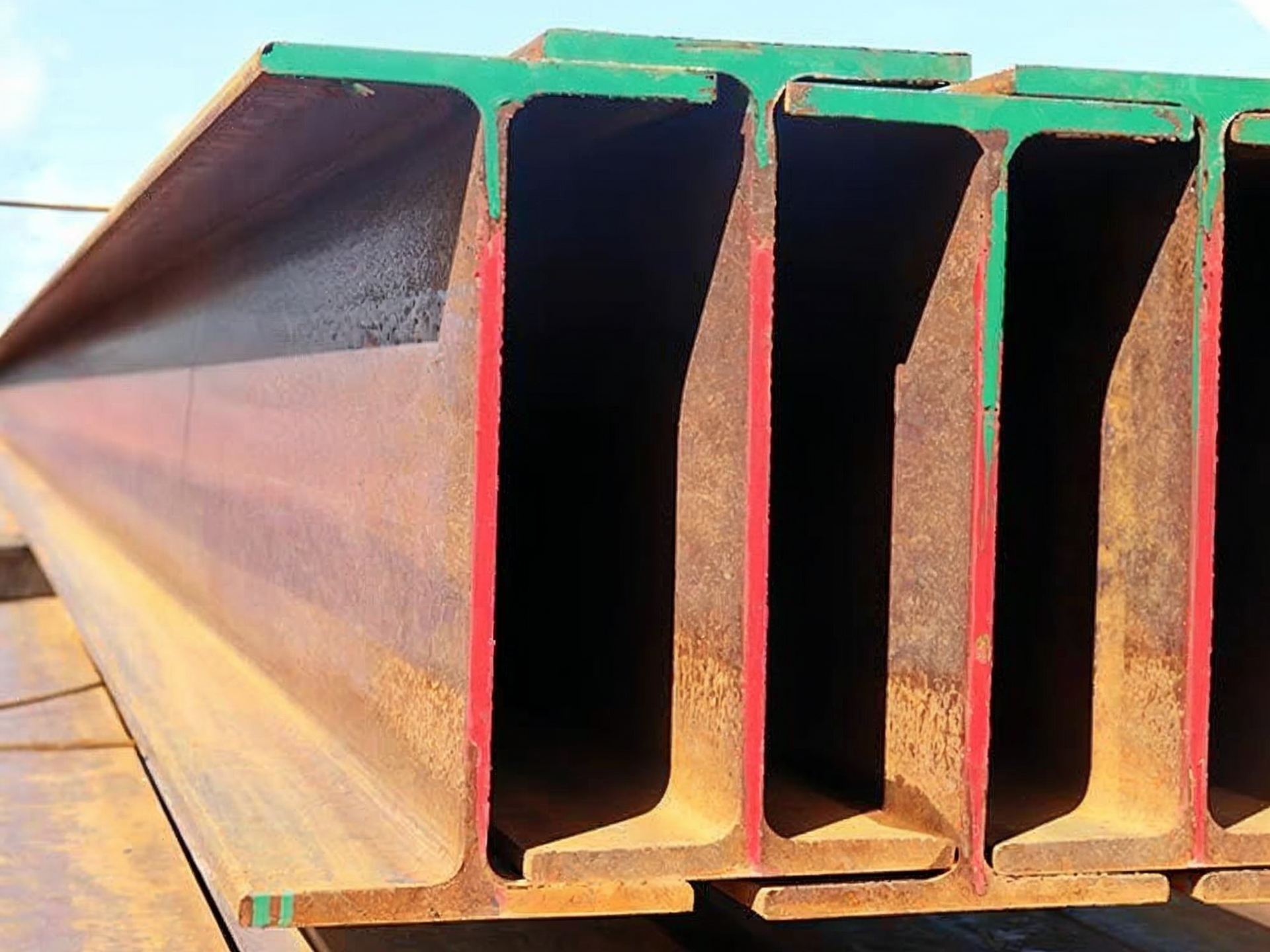 Stacked rusty steel beams with rectangular hollow sections against a bright sky
