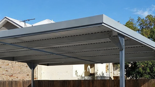 Large gray metal carport with a flat roof in a backyard, beside a fence and house.