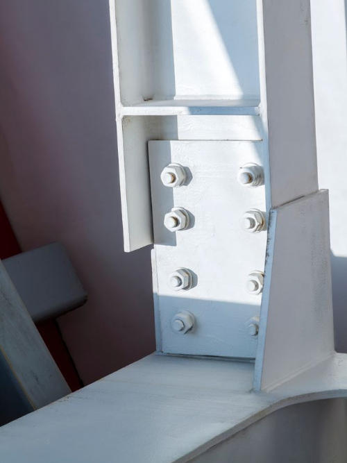 Close-up of a white metal beam joint with bolts and plates on a structural frame