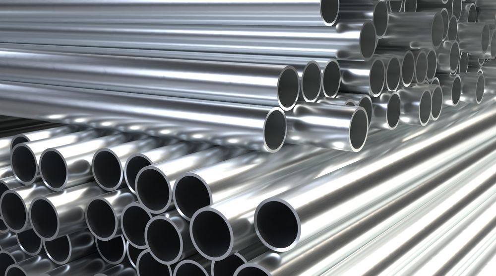 Stacked shiny metal pipes arranged in rows, showing open ends against a bright industrial background.