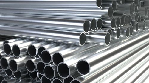 Stacked shiny metal pipes arranged in rows, showing open ends against a bright industrial background.
