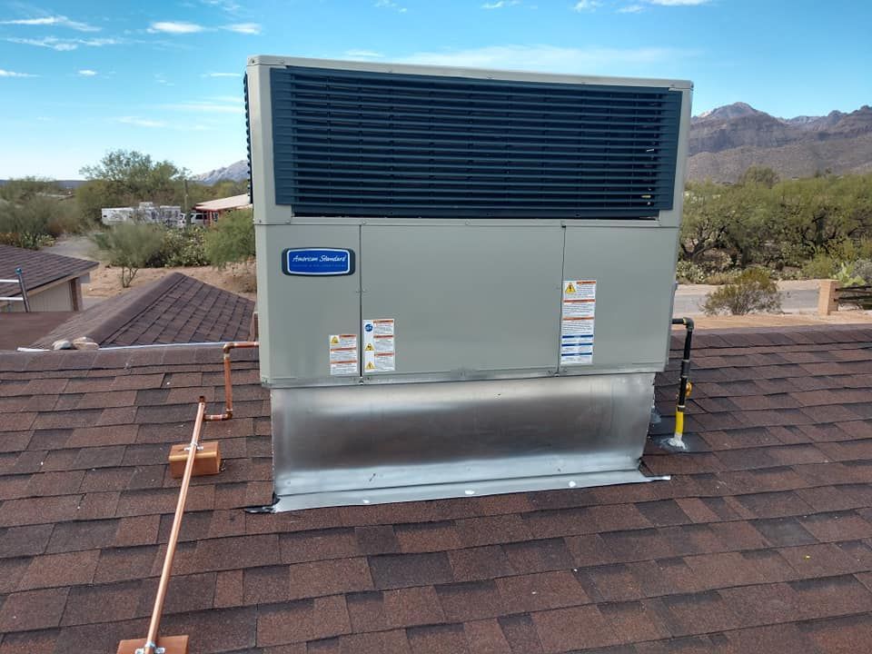 Metal rooftop HVAC unit with large vent, on a shingled roof against a desert mountain backdrop