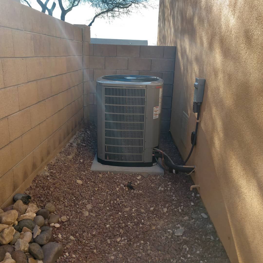 Outdoor HVAC unit in a narrow gravel side yard between tan block walls