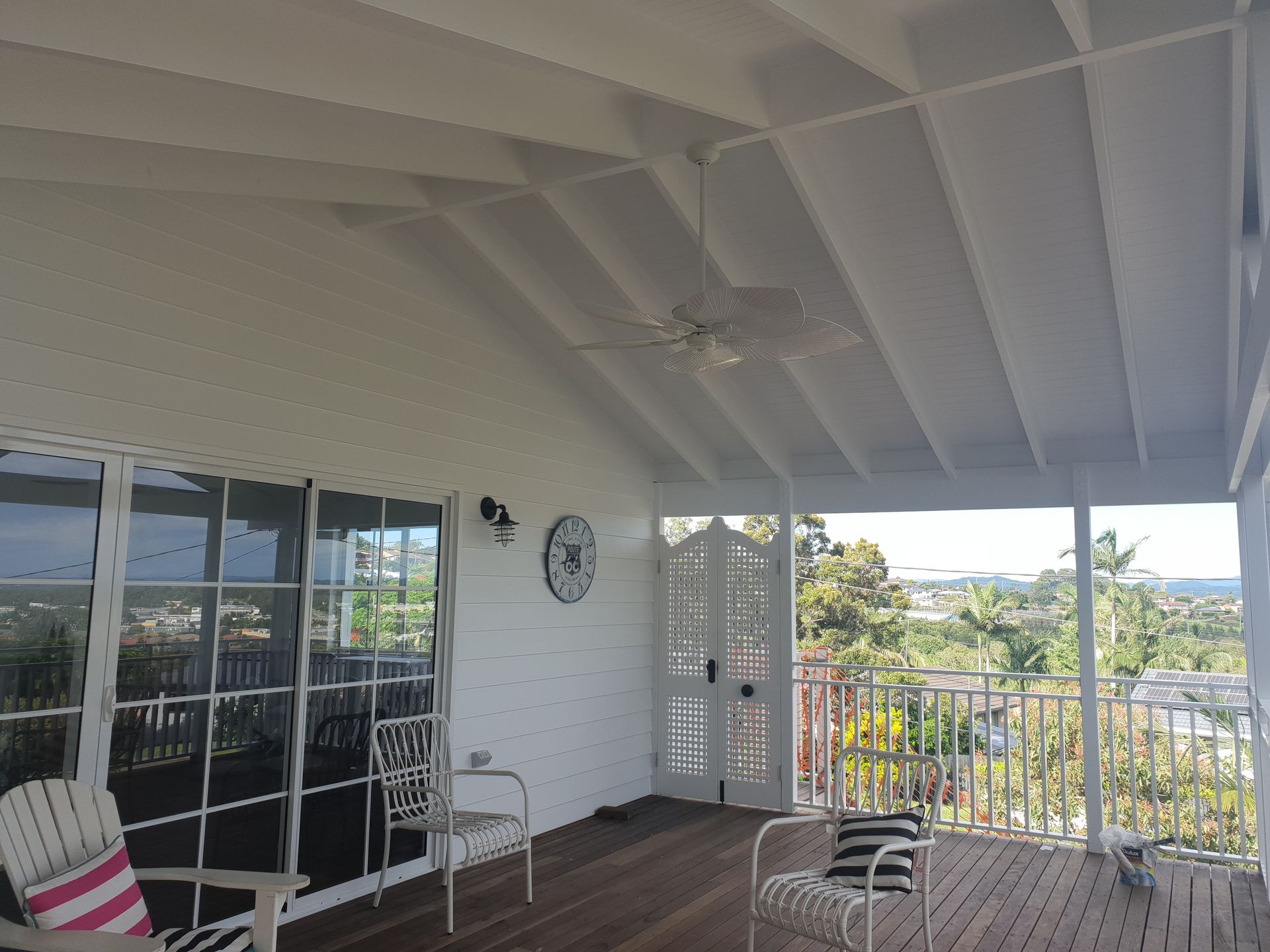 Covered porch with white ceiling, wicker chairs, glass doors, and a view of greenery and hills.