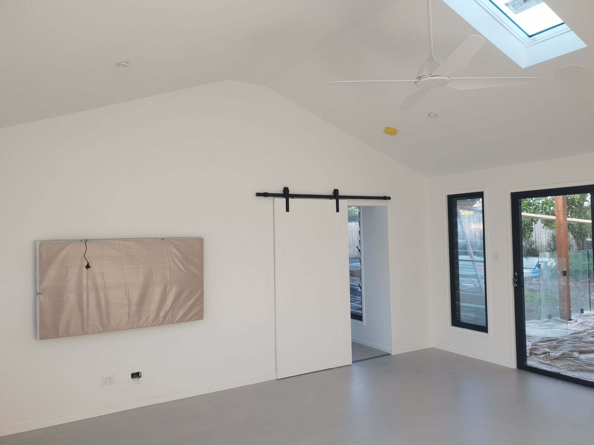 Minimal white room with large windows, skylight, and barn-style sliding door track