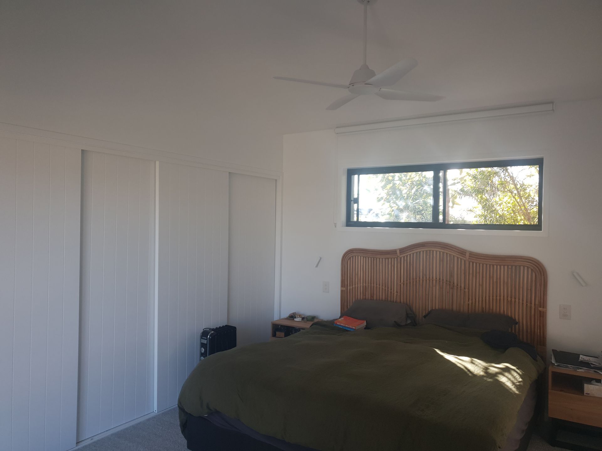 Bedroom with white walls, a wooden bed, green comforter, and a window above the headboard.