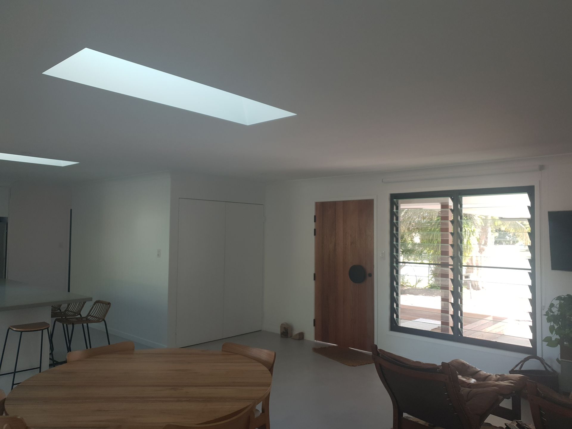 Bright modern room with round table, chairs, white walls, skylight, and large window by a wooden door
