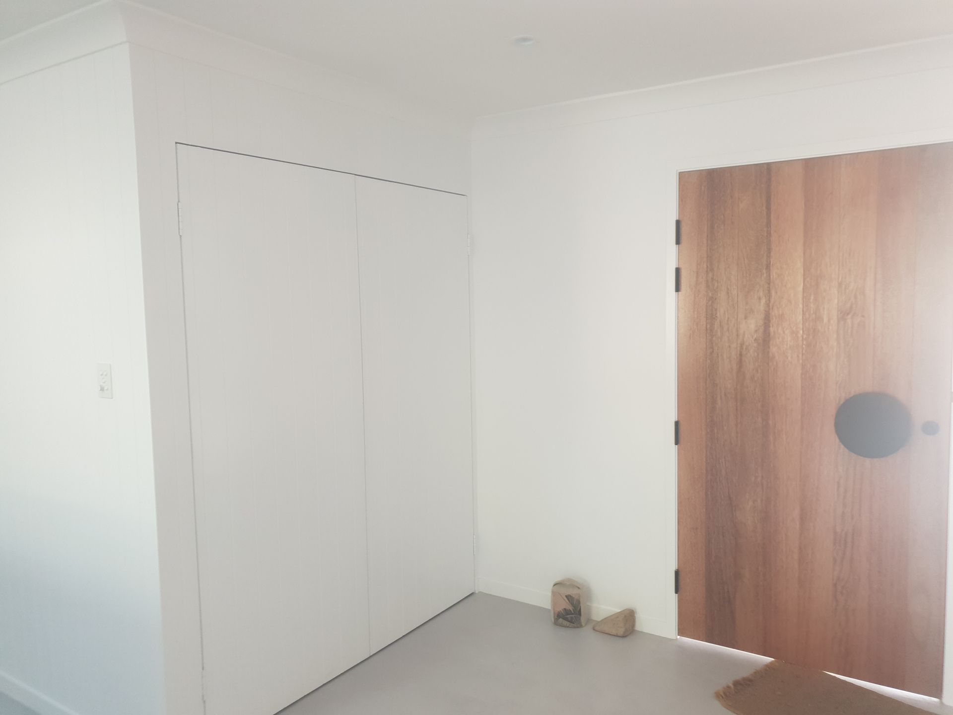 Sparse white room with a wooden door, closet doors, and a pair of shoes on the floor.