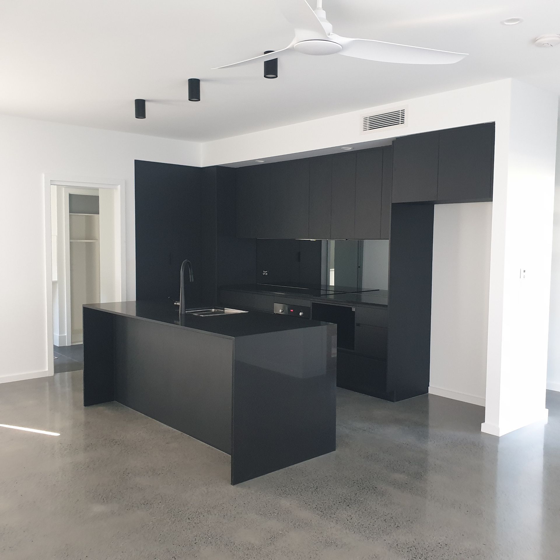 Modern black kitchen with island in a bright, empty room with white walls and concrete floor