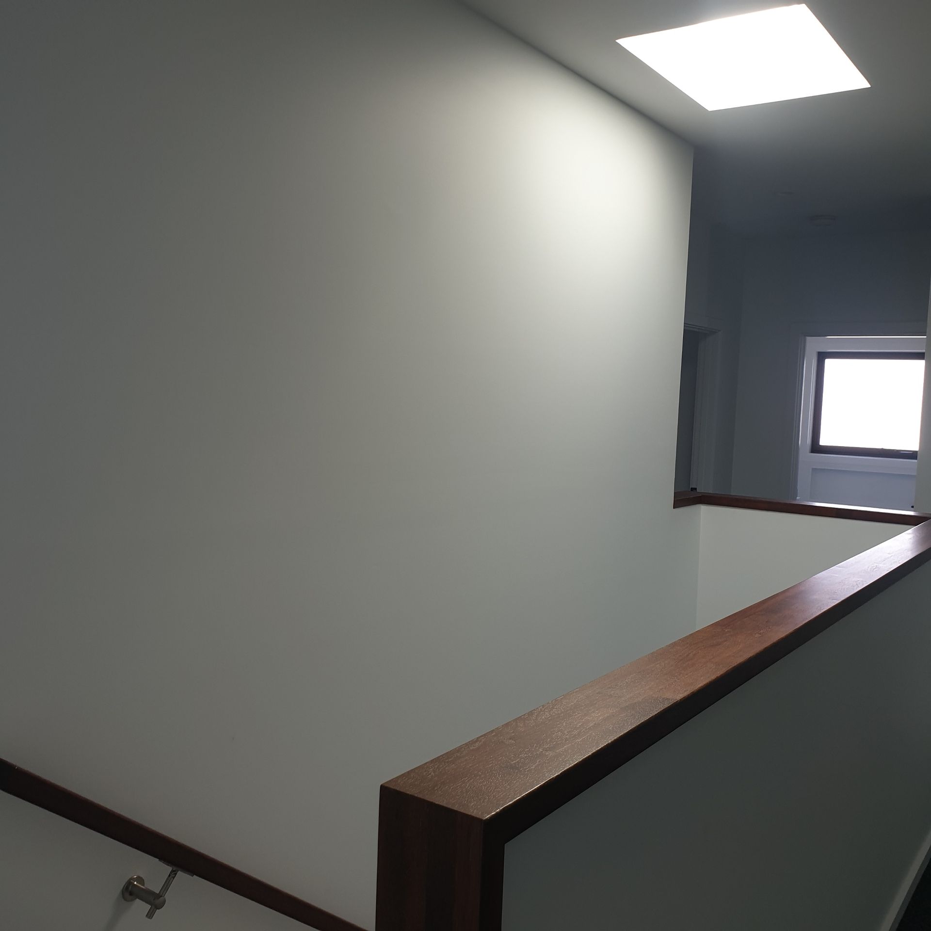 Indoor stairwell landing with gray walls, wood handrail, and a bright window below.