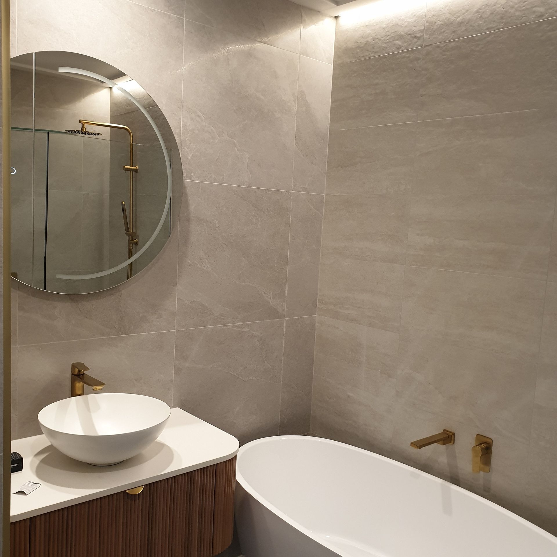 Modern bathroom with a round mirror, vessel sink, and freestanding white tub against gray tile walls