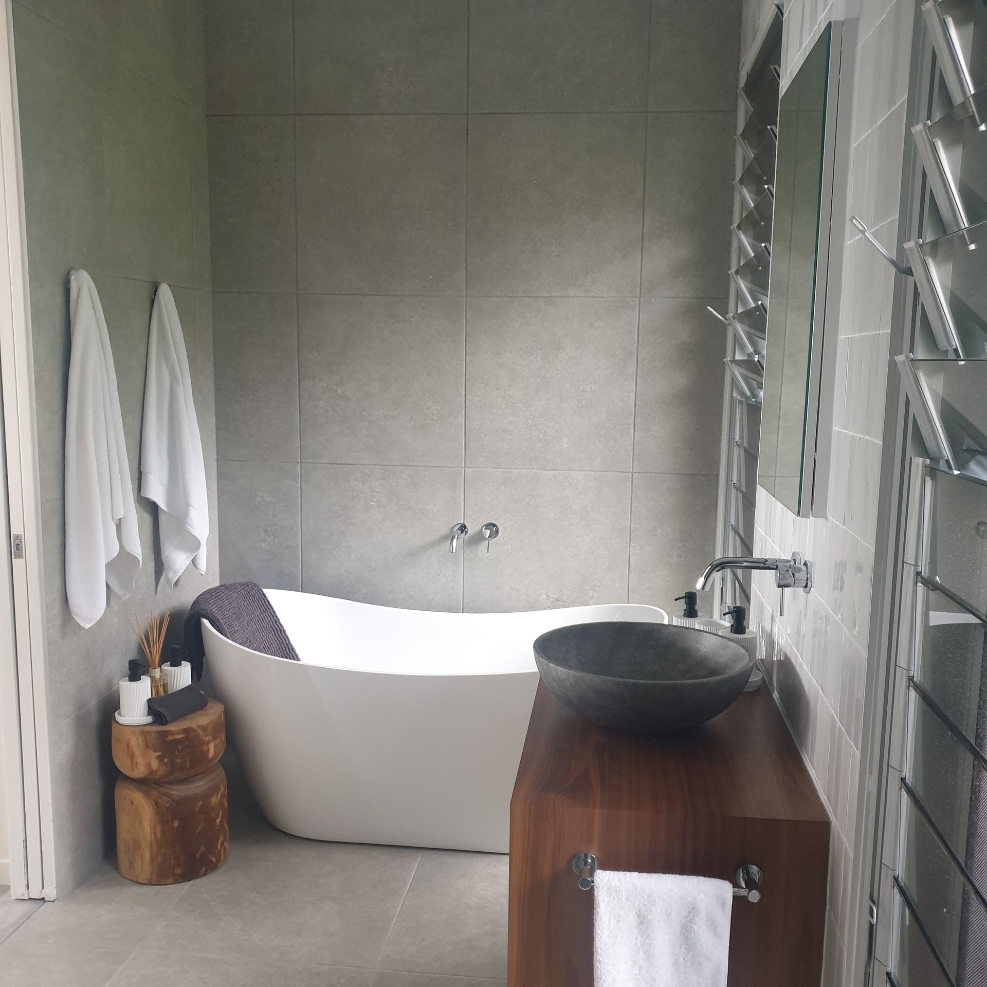 Modern bathroom with freestanding tub, wood vanity, towels, and tiled walls — Greg Pollard Building in Cabarita Beach, NSW