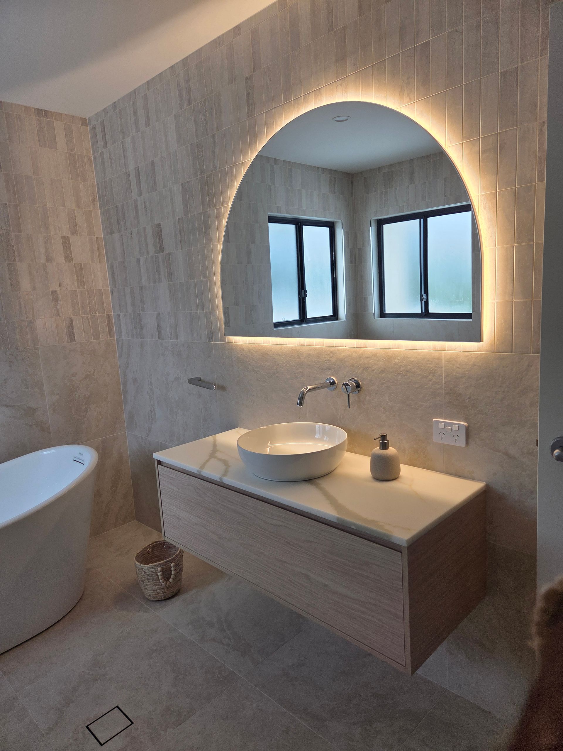 Modern bathroom with floating vanity, round mirror, and large windows in a textured stone interior