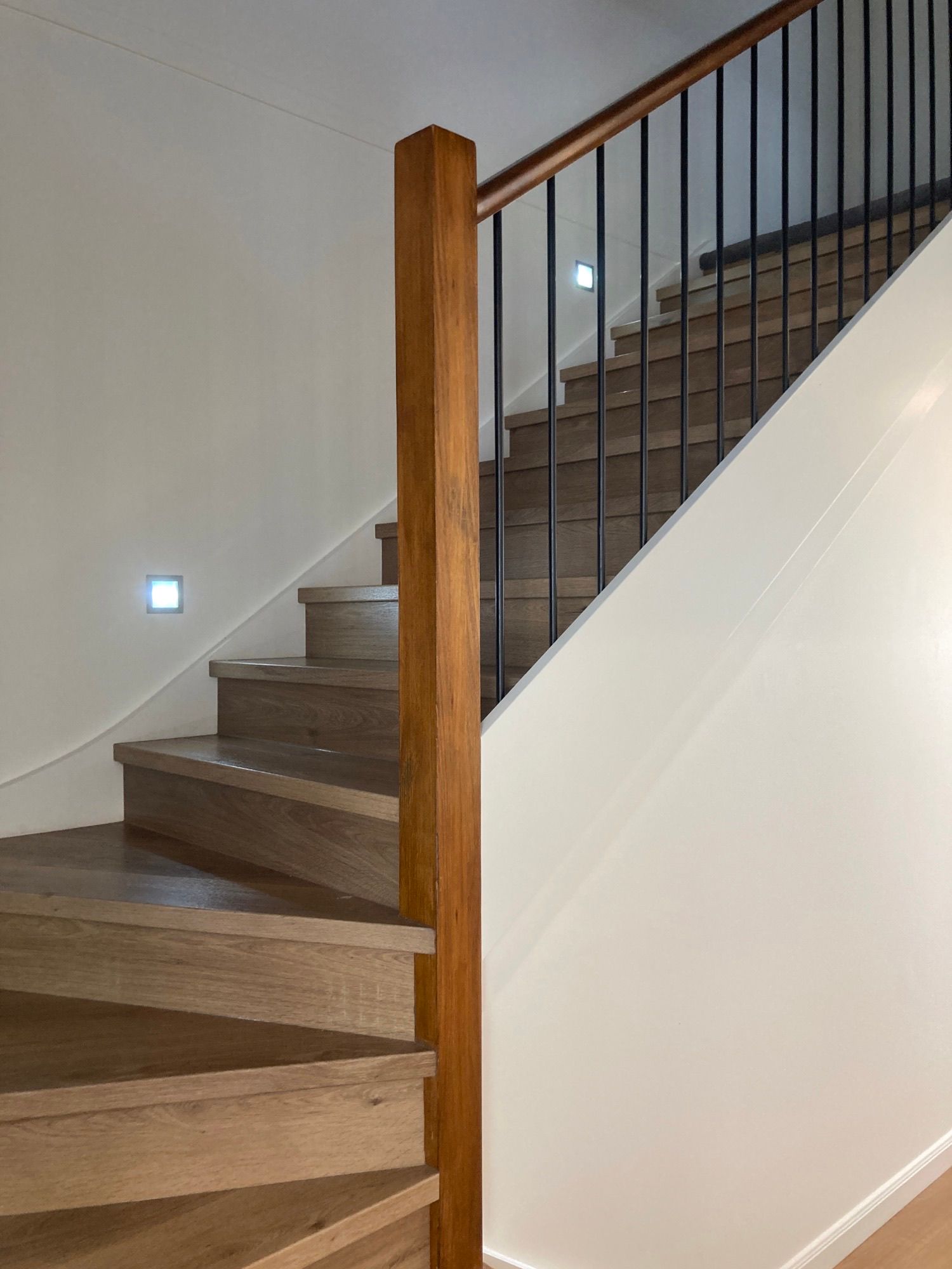Indoor staircase with wooden steps, black metal railing, and white walls