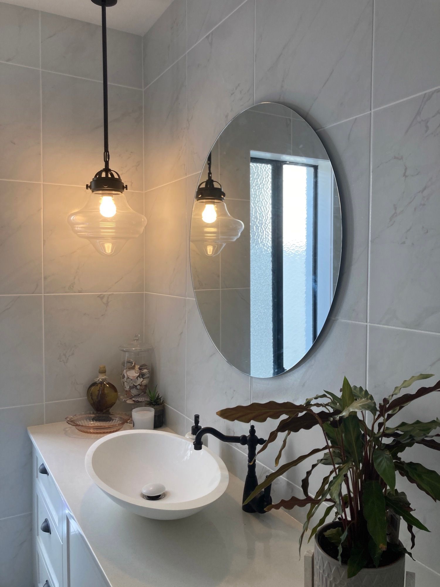 Modern bathroom vanity with round mirror, hanging lights, white sink, and potted plant