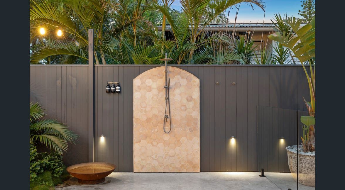 Modern front gate with stone arch, dark walls, and warm pathway lights at dusk