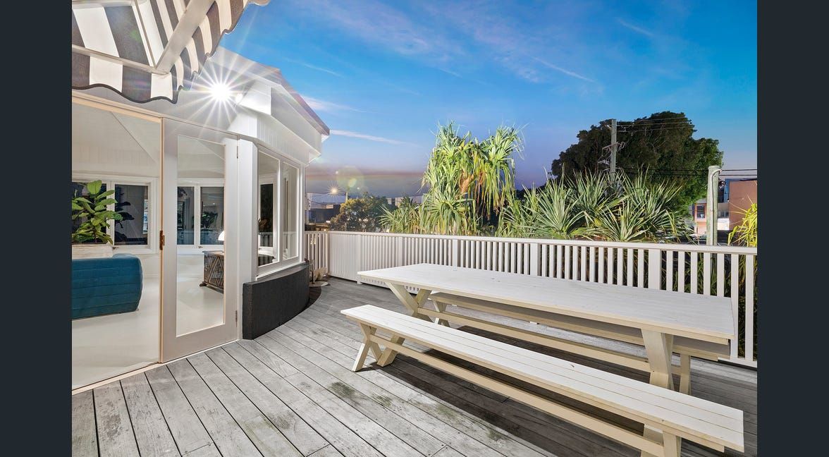 Modern patio with glass walls, outdoor table and chairs, and a cloudy sky reflected in the glass.