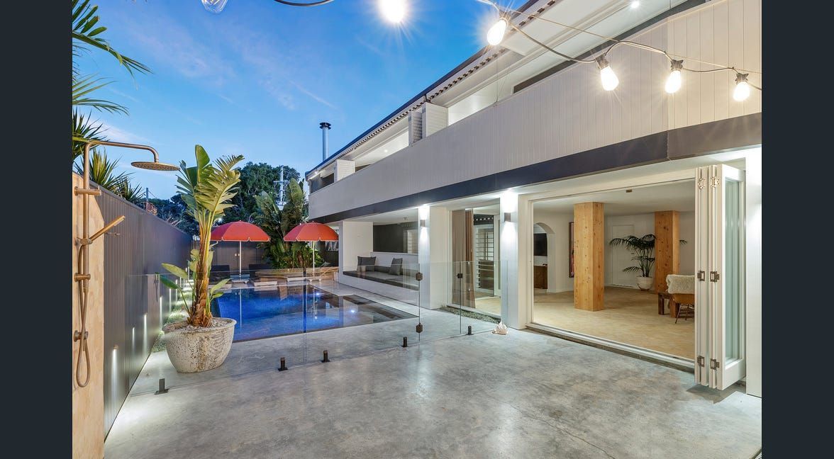 Modern patio with open sliding doors, blue pool, red umbrellas, and warm string lights at dusk