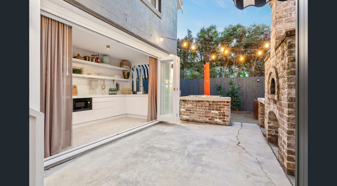 Modern patio beside a home with open kitchen doors, stone wall, and string lights at dusk