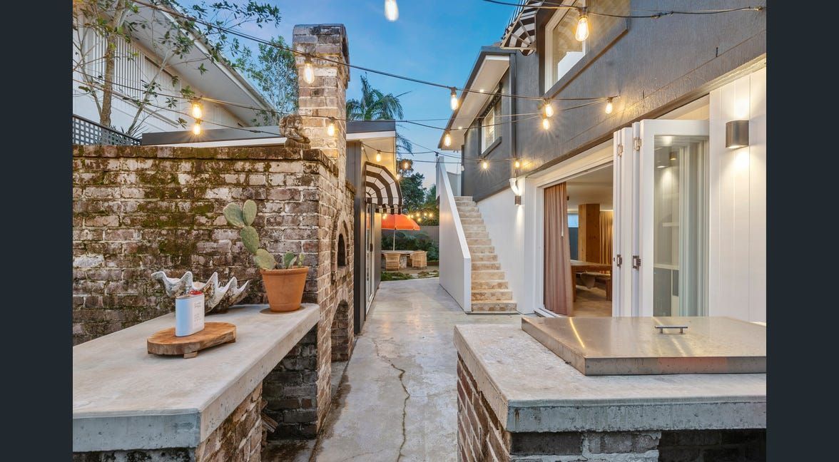 Narrow stone alley between two lit houses at dusk, with potted plants and a staircase on the right.