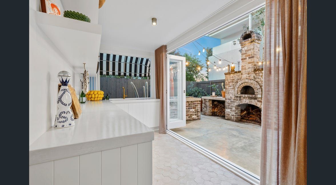 Bright white kitchen opening to a patio with stone fireplace and twilight outdoor seating