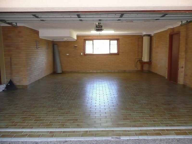 Empty unfinished room with wooden floor, brick walls, exposed beams, and a small window at the back