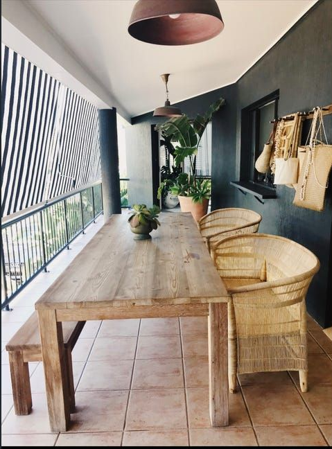 Covered patio with rustic wooden table, wicker chairs, terracotta floor tiles, and potted plants