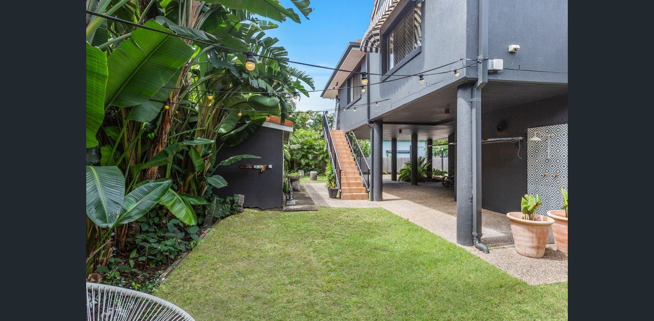 Backyard patio with green lawn, tropical plants, and a raised deck with stairs and seating area