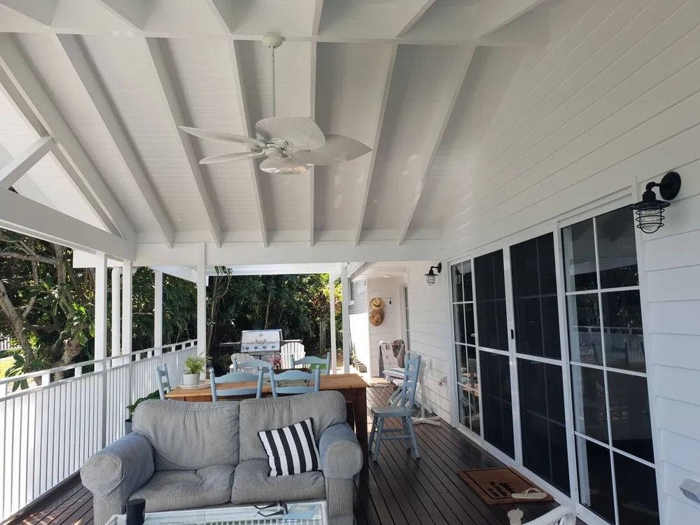 Covered Patio With White Beams, Gray Sofa, and a Dining Table Beside Sliding Glass Doors — Greg Pollard Building in Cabarita Beach, NSW