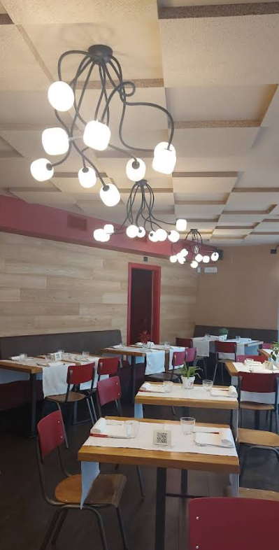 Interno del ristorante con tavoli apparecchiati per cenare, sedie rosse e lampade moderne.