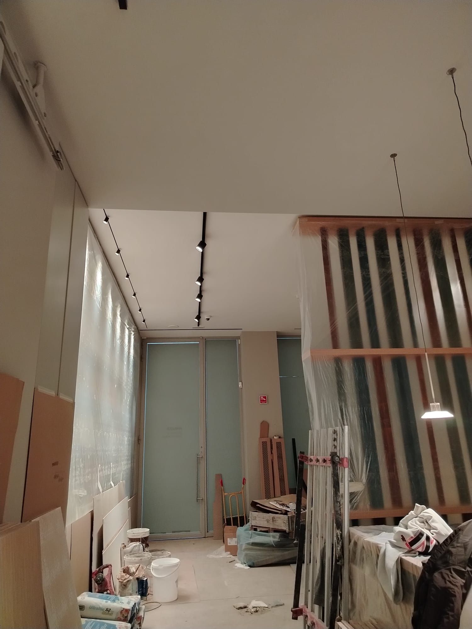 Interno di una stanza in costruzione con pareti nude, illuminazione a binario e una porta.