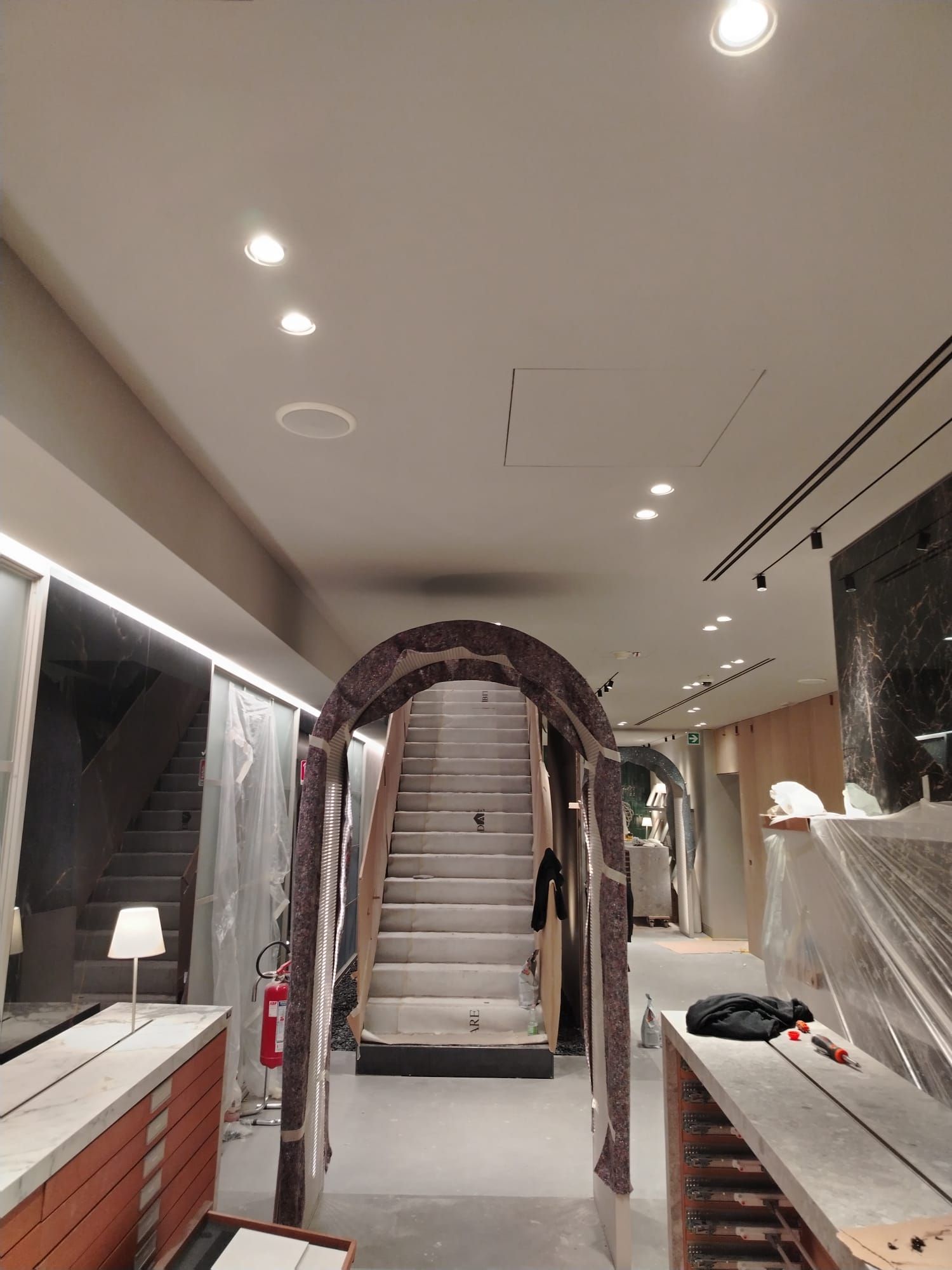 Interno di un negozio in costruzione con scale e una porta ad arco decorativa che conduce verso l'alto.