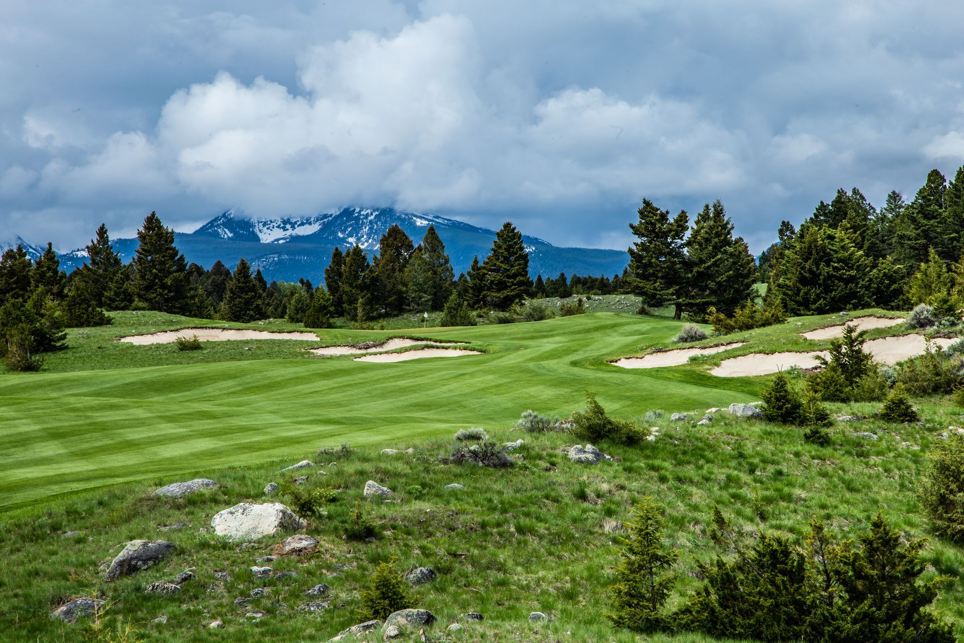 A golf course with mountains in the background and trees in the foreground.