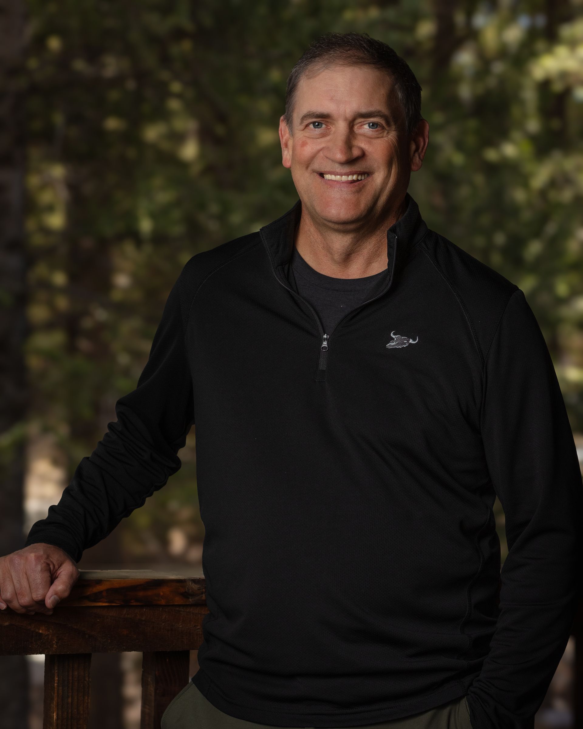 A man in a black sweater is leaning on a railing and smiling.