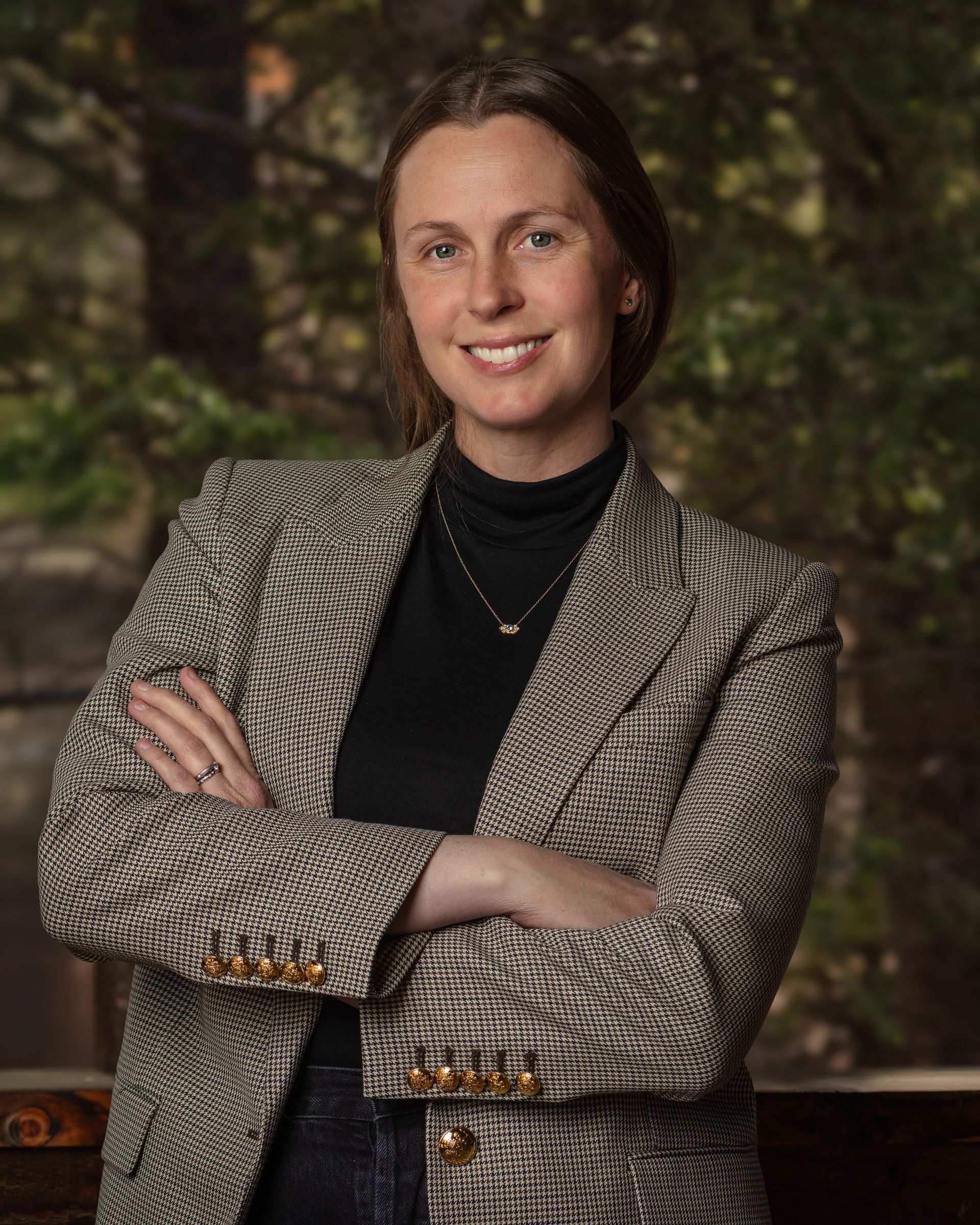 A woman in a plaid jacket and black turtleneck is standing with her arms crossed.